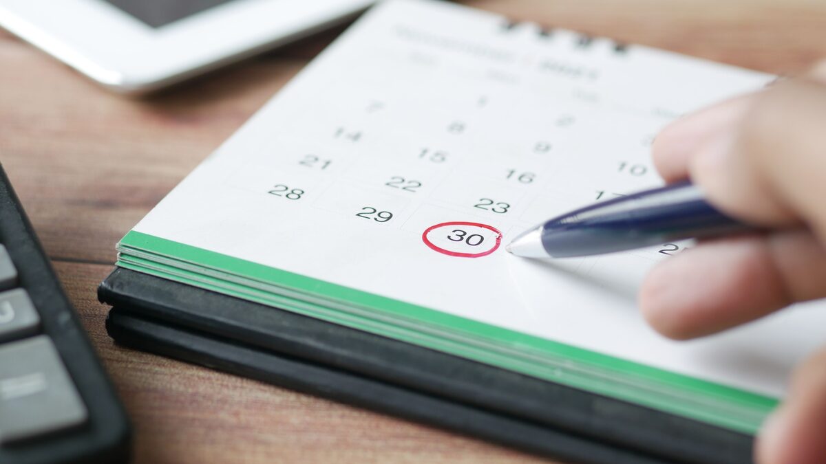 A date circled in red on a desk calendar, beside a calculator and tablet