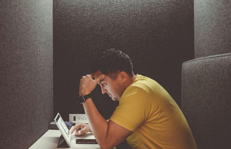 A business owner sitting alone at a laptop with his head in his hand